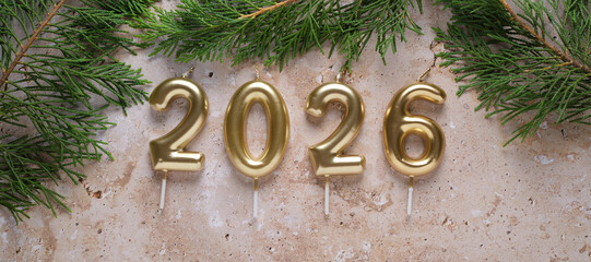 Celebratory golden 2026 candles surrounded by green pine branches on a textured surface