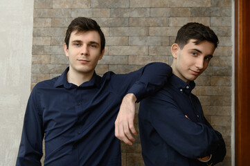 Fototapeta premium Two young men stand together in a room with stone walls while wearing dark shirts