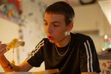caucasian teen eating pizza slice bedroom, warm lamp light, wearing black tracksuit and silver chain, focused expression, open pizza box on desk, posters on wall, latenight study break
