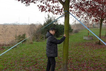 Child observing surroundings, Boy in outdoor neighborhood setting, Young boy rests beside tree trunk, Young boy in warm jacket and cap watching attentively near residential houses
