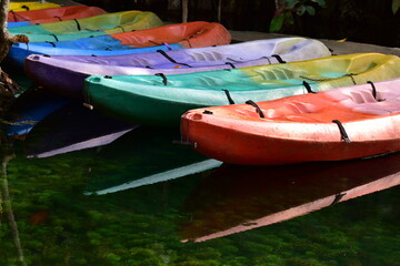 A brightly colored canoe floats on the water,A number of brightly colored kayaks float in the still water