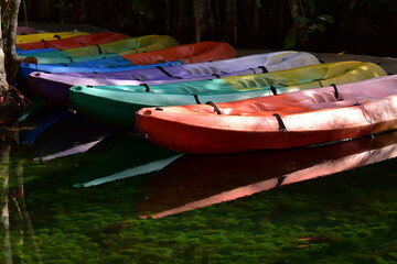 A brightly colored canoe floats on the water,A number of brightly colored kayaks float in the still water