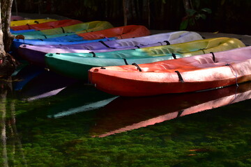 A brightly colored canoe floats on the water,A number of brightly colored kayaks float in the still water