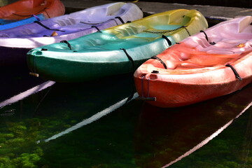 A brightly colored canoe floats on the water,A number of brightly colored kayaks float in the still water