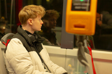 Contemplative Caucasian man gazing out window in tram, profile silhouette against city lights, wearing coat and scarf with backpack, quiet reflective mood, soft interior lighting and glass