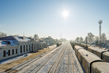 Winter railway station in the morning light. A snowy railway station with freight cars and tank cars. Tracks stretch to the horizon.