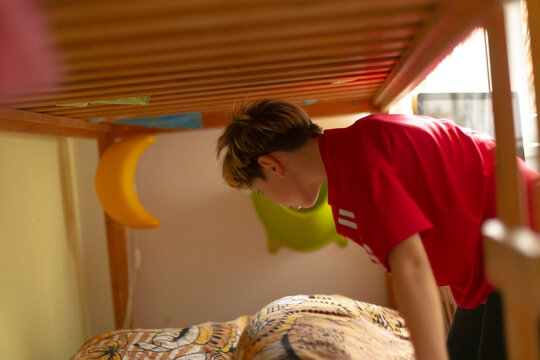 Young boy checks hidden area, Teen quietly searches secret spot beneath sleeping area, Young child stealthily examines concealed space underneath bed with comfort and curiosity