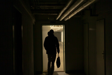silhouette stepping through bright doorway into warm yellow light, backlit threshold and strong contrast, escape or arrival narrative, pipes overhead create industrial frame, cinematic