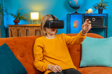 Caucasian teenager boy plays virtual reality game at home couch living room. Enthusiastically waves hands shows WOW emotion while sitting on sofa displaying excitement and enjoyment with VR technology