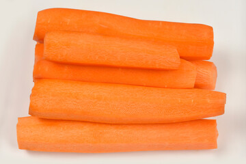 A pile of fresh peeled orange carrots is stacked horizontally on a white cutting board surface