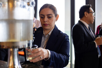 professional woman in business attire pouring a drink from a dispenser at a corporate networking event, highlighting professionalism and event hospitality