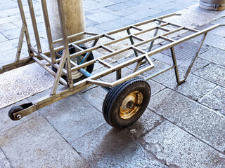 Metal luggage cart on cobblestone street with two wheels and stand