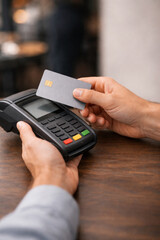 Hand holding credit card, paying at card terminal, in vertical