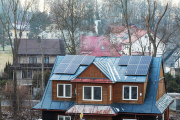 RABA WYZNA, POLAND - DECEMBER 27, 2025: Nasty grey smoke from burning garbage in the home furnace comes out of the house's chimney. Another house has clean energy from photovoltaic panels.