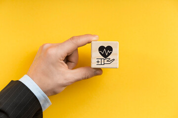 Health insurance concept. Healthcare, finance and medical service. Wooden cube block with hand holds heart pulse, heartbeat lone and cardiogram symbol. Healthcare, medical background and copy space.