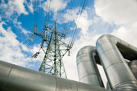 a pipeline and a power transmission tower against a blue sky and clouds