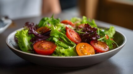 A vibrant bowl of fresh mixed green salad with juicy cherry tomato halves presented in a dark ceramic bowl