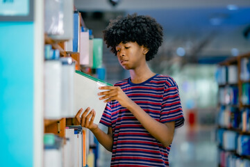 Young Blacjk University student choosing academic book from library shelf showing higher education research study preparation focused learning environment campus life.