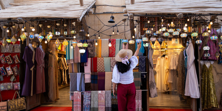 Tourist woman enjoying traditional market shopping at Istanbul bazaar with Turkish glass lamps, scarfs and colorful textiles on display