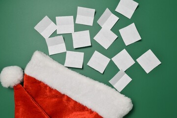 White blank sheets of paper and a Santa hat on a green background. Secret Santa concept