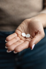 Close-up of female hand holding two white round pills with score line, concept of medication and pharmaceutical treatment