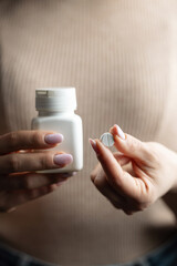 Close-up of female hands holding white pill bottle and single white round pill with score line, concept of medication and pharmaceutical treatment