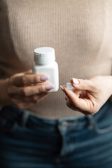 Close-up of female hands holding white pill bottle and single white round pill with score line, concept of medication and pharmaceutical treatment