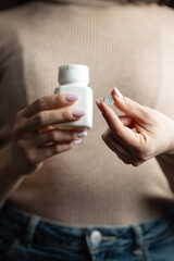 Close-up of female hands holding white pill bottle and single white round pill with score line,...