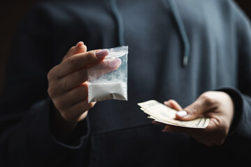 Close-up of female hands holding cash and transparent plastic bag with white narcotic powder, concept of drug abuse and drug trafficking