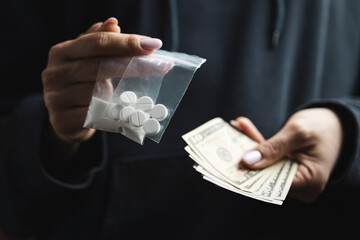 Close-up of female hands holding cash and two transparent plastic bags with white narcotic powder and white pills, concept of drug abuse and drug trafficking