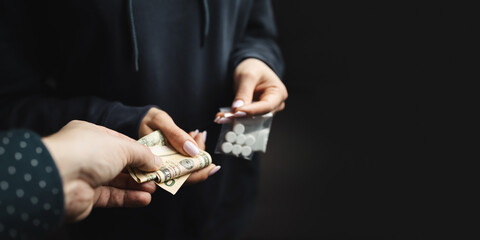 Close-up of addicted person hands paying cash to buy two transparent bags with narcotics, white pills and powder from drug dealer, concept of drug abuse and drug trafficking