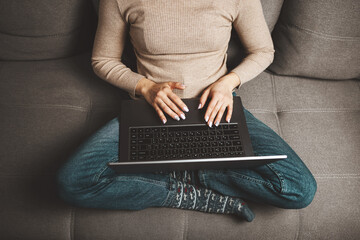 Woman sitting cross-legged on couch using laptop at home, concept of freelance work, remote job, online learning and e-commerce