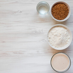 Flour in a bowl and water in a glass bottle on a wooden table with large copy space and natural light. Suitable for recipe pages, food blogs, bakery websites, presentations and editorial layouts.