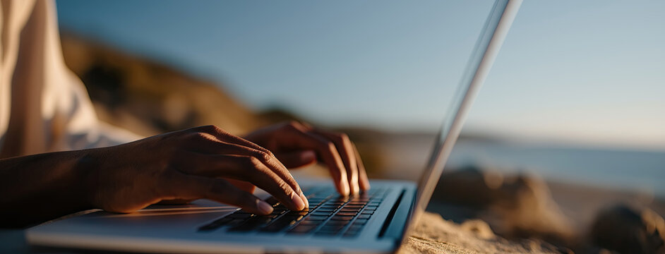 Person types on laptop by seaside, representing remote work freedom and flexibility.