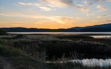 Obraz premium Minimalist dusk landscape featuring tall dry meadow grass, a reflective lake, and distant forested hills. 