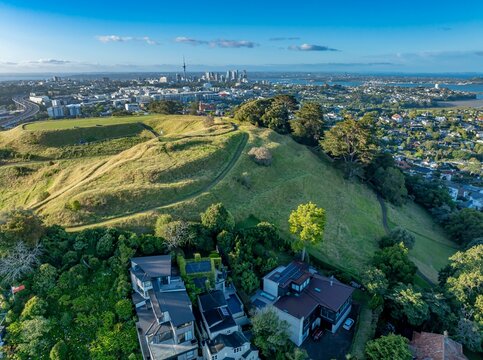 Aerial view of Remuera, Auckland, New Zealand, showcasing the city skyline with the Sky Tower, lush green hills, and residential areas. The image highlights urban living.
