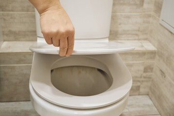 Hand lifting white toilet lid, focusing on hygiene in modern bathroom
