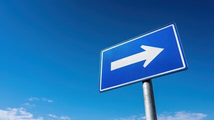 A blue traffic sign with a white right arrow stands on a metal pole against a clear blue sky dotted with small clouds.