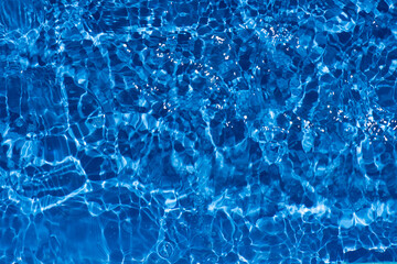 Blue water with ripples on the surface. Defocus blurred transparent blue colored clear calm water surface texture with splashes and bubbles. Water waves with shining pattern texture background.