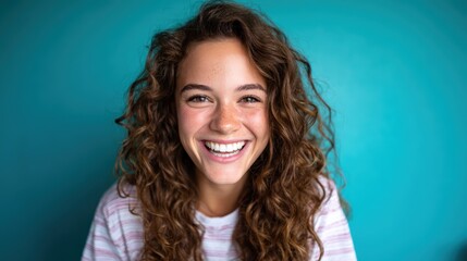 A cheerful young woman with curly hair beams joyfully against a vibrant turquoise background, exuding positivity and warmth that invites viewers to share in her happiness.