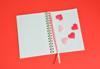 Open Notebook with silk Hearts and Pink Ribbon on Red Background flat lay