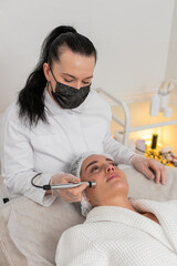 Injection-free mesotherapy or electroporation. Beautician doctor makes client woman face therapy in...