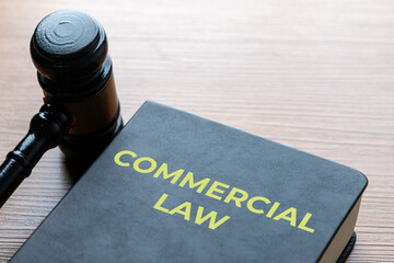 A wooden judge&rsquo;s gavel next to a black book titled COMMERCIAL LAW. Corporate justice, legal authority, business regulations concept.