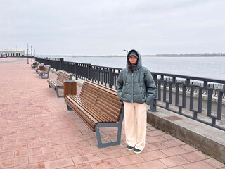 A person stands by the river with benches around on a cold and cloudy day