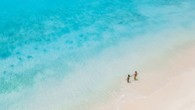 A couple strolls hand in hand along the pristine, white sands of Klein Curacao, surrounded by crystal-clear waters. Drone view of a couple of men and women on vacation walking on the beach in Curacao