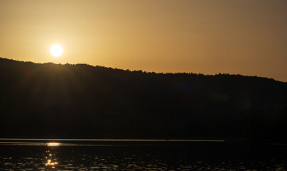Golden hour over a quiet lake with the sun shining on reflective water and silhouetted hills on the horizon. Evocative sunset landscape with warm light and calm mood, suited for backgrounds.