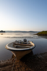 A white fishing boat tied to the shore provides a focal point in the foreground, while warm morning light illuminates the water's surface.