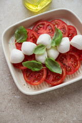 Caprese with bocconcini cheese, ripe tomato slices and fresh green basil, vertical shot on a beige stone surface, middle closeup