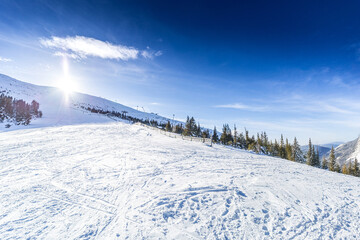 A wide scenic shot of a groomed ski slope in the Low Tatras, Slovakia, under a dramatic cloudy sky during twilight, featuring snow-covered ridges and evergreen forests.