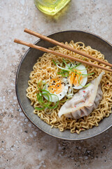 Plate of ramen with steamed dumpling, boiled egg and spring onion, vertical shot on a beige granite background